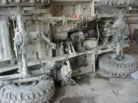 1992 Ford Bronco - Underside view of a dust-caked leaf-sprung solid-axle chassis lying on its side on a shop floor, showing the frame rails, transfer case and…