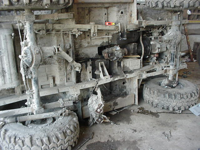 Mud-caked leaf-sprung 4x4 chassis on its side showing transfer case, driveshafts and knobby tires