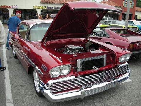 1998 Ford Crown Victoria - A classic red 1958 Chevrolet Bel Air is displayed with its hood open, revealing the engine, at an outdoor car event.