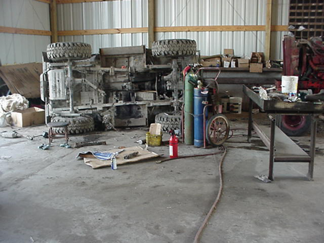 Stripped small 4x4 chassis rolled on its side in a shop next to a torch cart