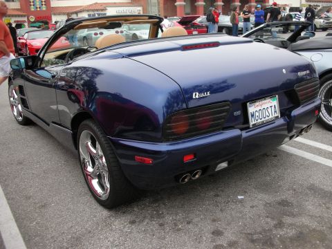 1998 Ford Crown Victoria - A blue Qvale Magesta convertible is parked in a lot with other vehicles visible.