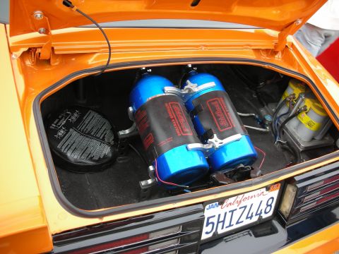 1998 Ford Crown Victoria - The trunk of an orange car reveals twin blue nitrous oxide tanks and yellow Optima batteries, with a California license plate visible.