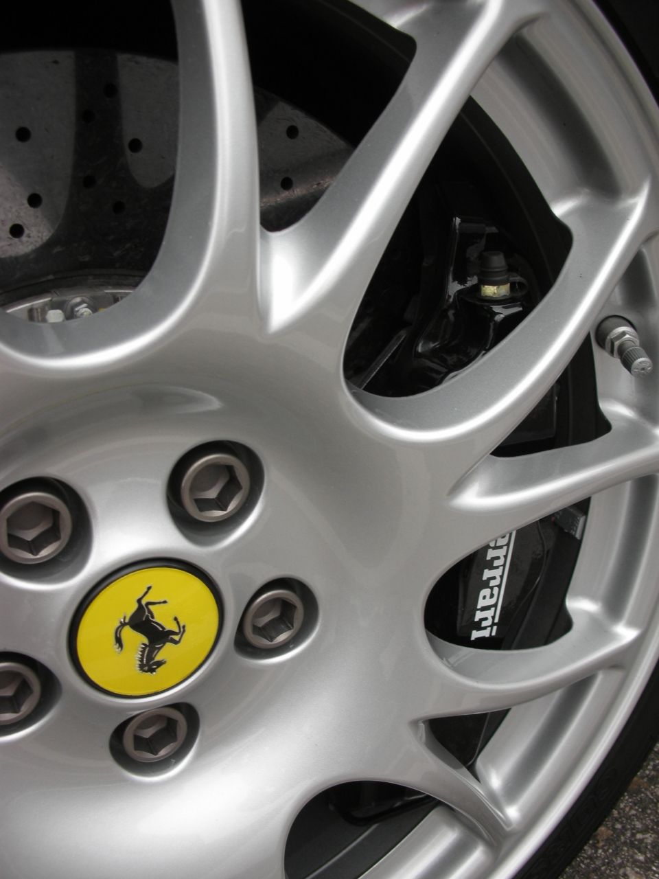 Silver multi-spoke alloy wheel with yellow Ferrari center cap and branded brake caliper