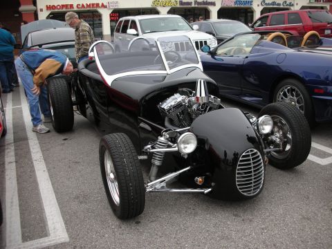 1998 Ford Crown Victoria - A custom black hot rod with an exposed V-twin engine is parked next to other vehicles.