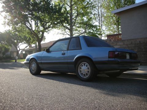 1990 Ford Mustang - A blue 1990 Ford Mustang coupe is parked on the side of a street in a suburban neighborhood.