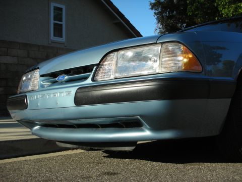 1990 Ford Mustang - Close-up of the front of a light blue 1990 Ford Mustang, showing the headlights and bumper.