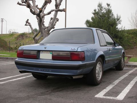 1990 Ford Mustang - Rear view of a light blue coupe with a 'Mustang' badge, parked in a lot.