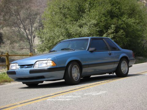 1990 Ford Mustang - A blue 1990 Ford Mustang is shown from the front three-quarter view on a paved road.