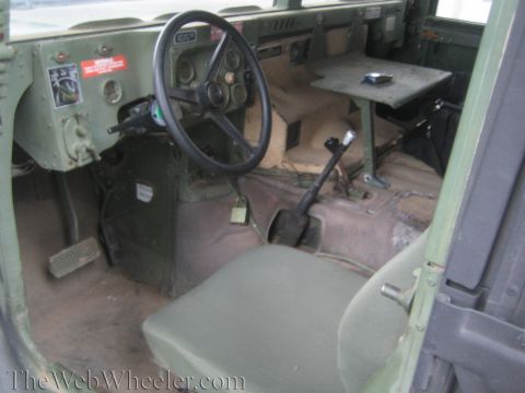 1990 Ford Bronco - Spartan military Humvee interior with an olive-green dashboard, center transmission hump, floor shifter and worn bench seat.