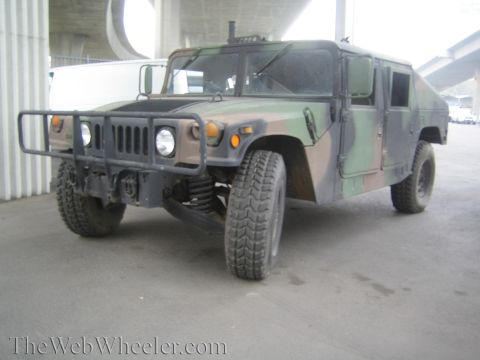 1990 Ford Bronco - Woodland-camouflage military Humvee with brush guard and large off-road tires parked beneath a concrete highway overpass.
