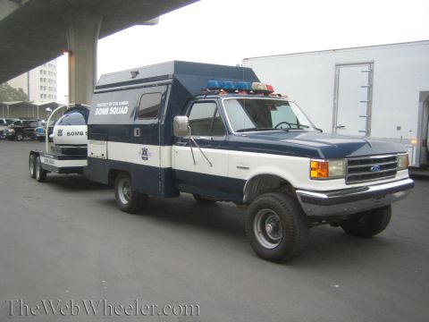 1990 Ford Bronco - District of Columbia Bomb Squad Ford dually box truck with light bar tows equipment under a highway overpass.