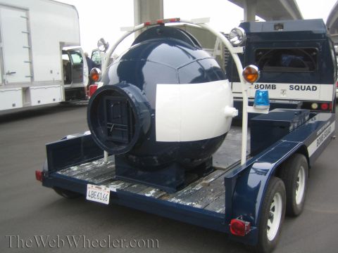 1990 Ford Bronco - Rear three-quarter view of a navy-and-white bomb containment sphere mounted on a tandem-axle Bomb Squad trailer.