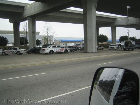 1990 Ford Bronco - Marked police cruisers and other vehicles staged along a roadway under a concrete overpass, shot through a side window.