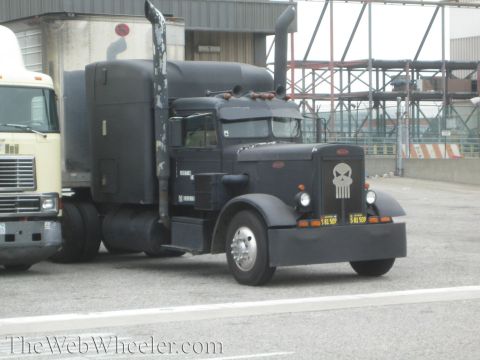 1990 Ford Bronco - Matte-black classic Peterbilt sleeper semi with a white skull painted on its grille, parked at an industrial yard.