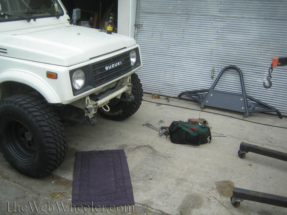 White 1987 Suzuki Samurai front view, modified with large tires and aftermarket bumper, parked on concrete