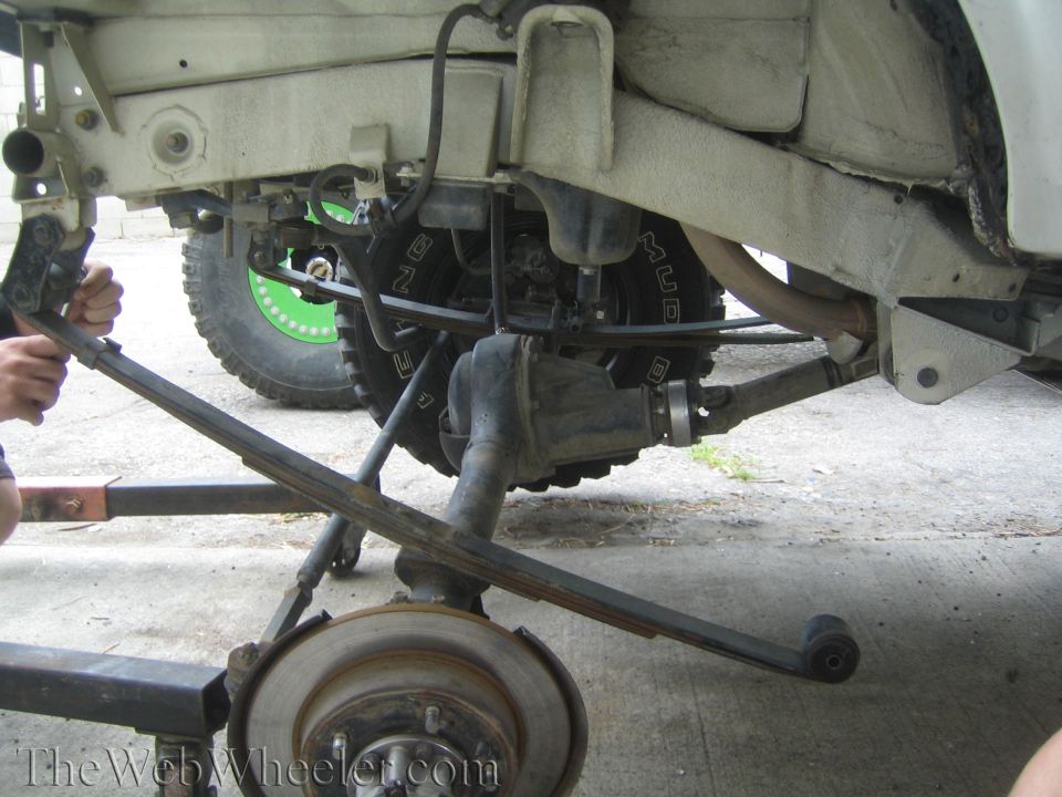Removed leaf spring pack held under jacked-up 4x4 with solid axle, diff and brake rotor