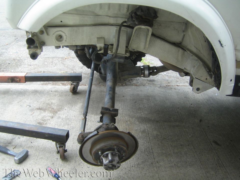 Solid front axle with differential and brake rotor removed from white 4x4 on concrete
