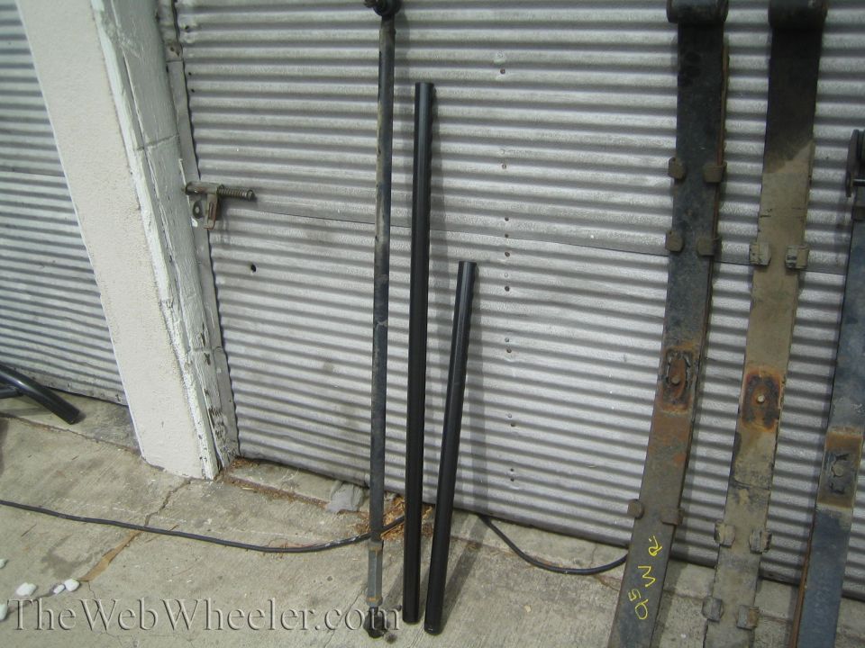 Steel tubing and rusty leaf spring packs leaning against a corrugated garage door