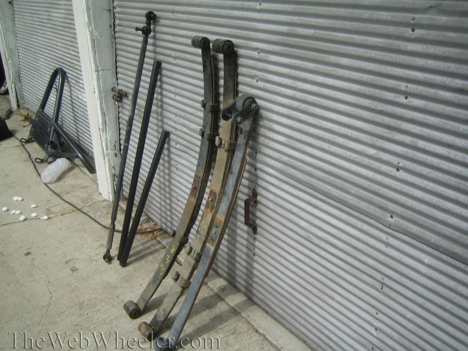 Leaf spring packs, shocks and tie rod leaning against corrugated metal door