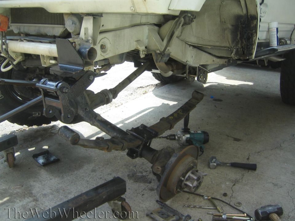 Underside of white vehicle with leaf spring, brake rotor and impact wrench during suspension work