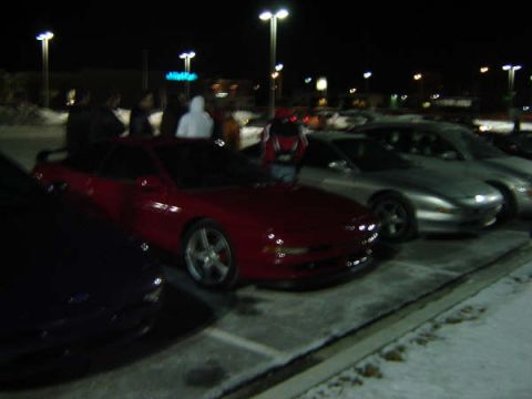 1993 Ford Probe - A red 1993 Ford Probe is parked in a lot with snow on the ground, with other vehicles and people visible.