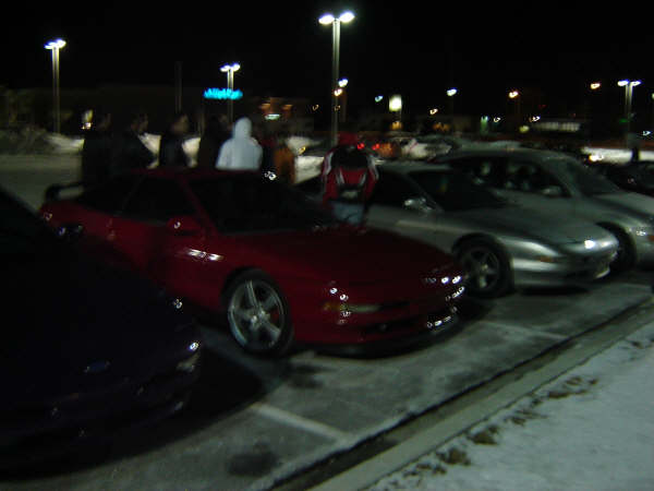 Red 1993 Ford Probe coupe parked in a snowy lot at night, front 3/4 view