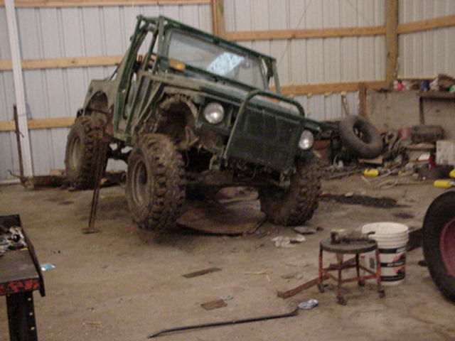 Green caged soft-top 4x4 on a jack stand in a pole barn shop with muddy knobby tires