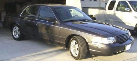 2005 Ford Crown Victoria - A dark gray Ford Crown Victoria is parked in a garage next to a white pickup truck.