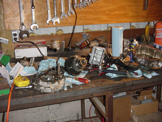 Workbench cluttered with transmission internals, gears and tools below a wrench rack