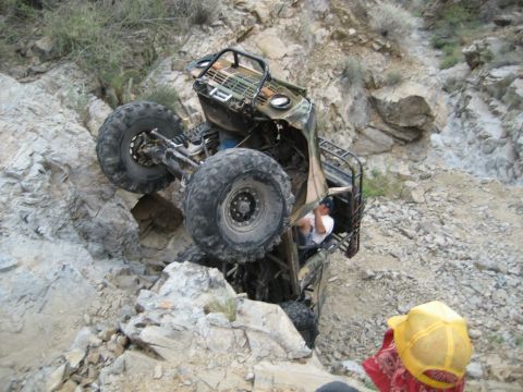 1966 Ford Bronco - An off-road vehicle is overturned on its side amidst a rocky, mountainous terrain, with a person visible inside the cabin.