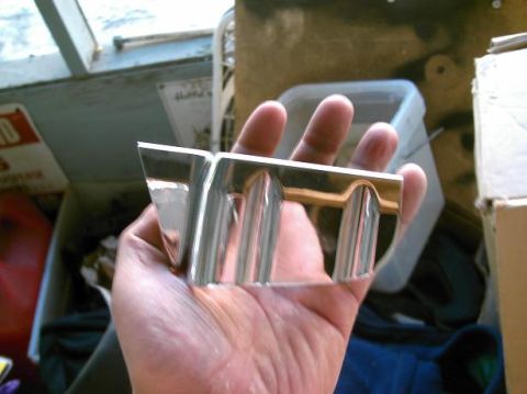 1986 Ford Bronco - Chrome emblem with vertical bars is held in a hand, with a blurred background of storage items.