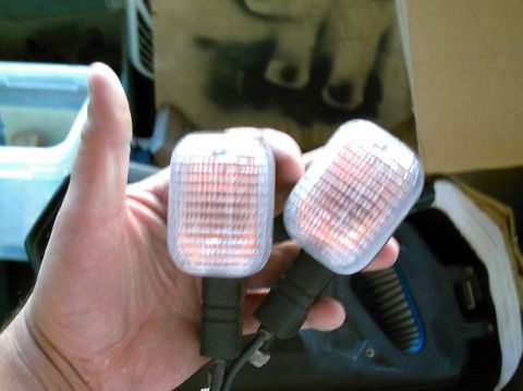 1986 Ford Bronco - Two amber turn signal lights are held in a hand, with a blurred background.