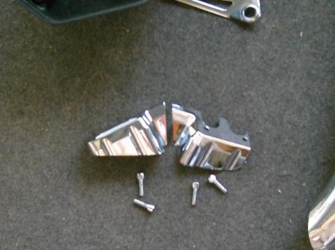 1986 Ford Bronco - Two chrome-plated trim pieces, possibly from a motorcycle or car, lie on a dark, carpet-like surface with several screws.