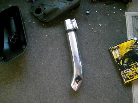 1986 Ford Bronco - A chrome exhaust pipe and a Buell '99/'00 Cyclone M2 service manual are laid out on a carpeted surface.