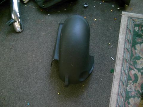 1986 Ford Bronco - A single black plastic fender part is visible on a carpeted floor next to a rug.