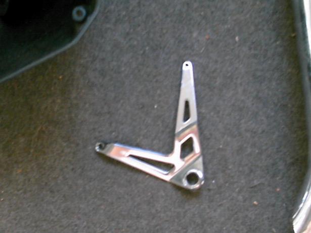 Chrome-plated metal bracket with triangular cutouts, lying on dark carpet