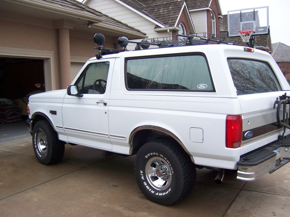 White Ford Bronco SUV with roof rack and aftermarket lights, parked in driveway