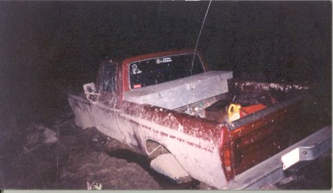 1992 Ford Bronco - Night flash photo of a two-tone red and white pickup buried to the axles in mud, shot from the rear three-quarter with the tailgate and chr…