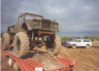 1992 Ford Bronco - Scanned print of an olive-drab flat-fender military-style 4x4 with an exposed roll cage and brush-guard front bumper, chained down on a red…