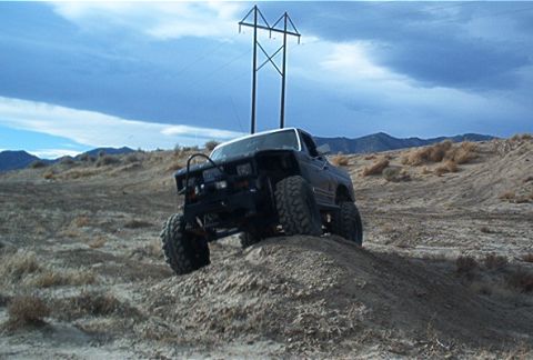 1986 Ford Bronco - This heavily modified SUV is shown off-road, navigating a steep dirt incline with large tires.