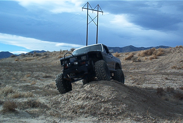 Modified SUV with large tires climbing a dirt mound under a power line