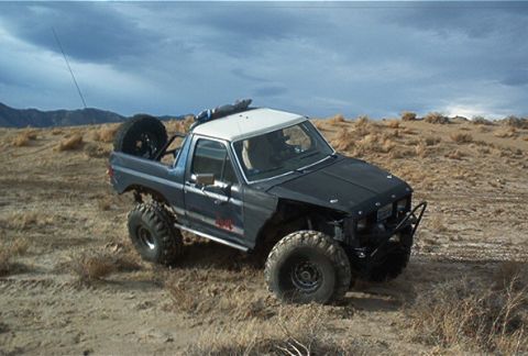 1986 Ford Bronco - This modified Ford Bronco navigates a desert landscape under a cloudy sky.