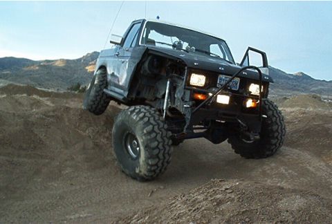 1986 Ford Bronco - This heavily modified 1986 Ford Bronco is captured mid-climb on a dirt trail, its off-road capabilities.