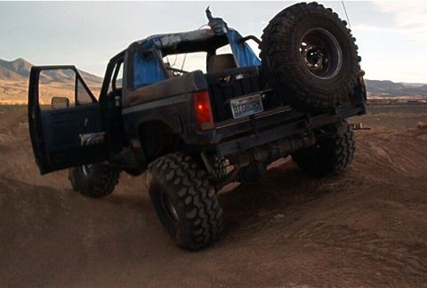 1986 Ford Bronco - This modified Ford Bronco is shown off-road with its driver's side door open and a spare tire mounted on the back.