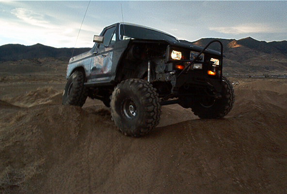 Dark blue Ford Bronco with large tires and a brush guard on a dirt hill