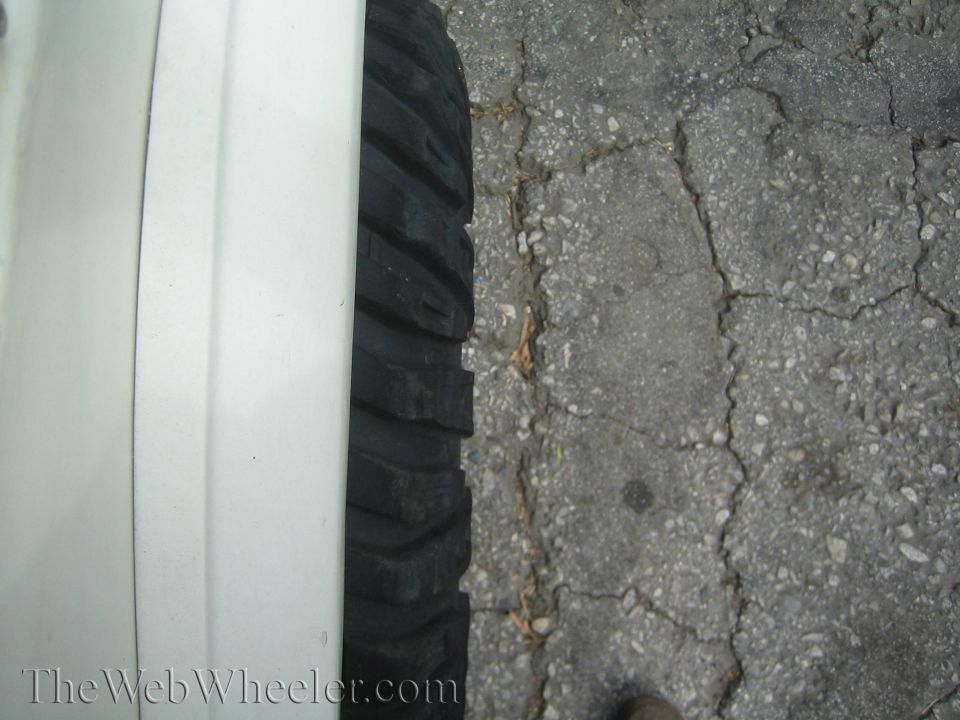Overhead close-up of mud-terrain tire tread next to white fender lip on asphalt