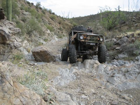 1966 Ford Bronco - A modified 1966 Ford Bronco navigates a challenging rocky off-road trail in a desert environment.