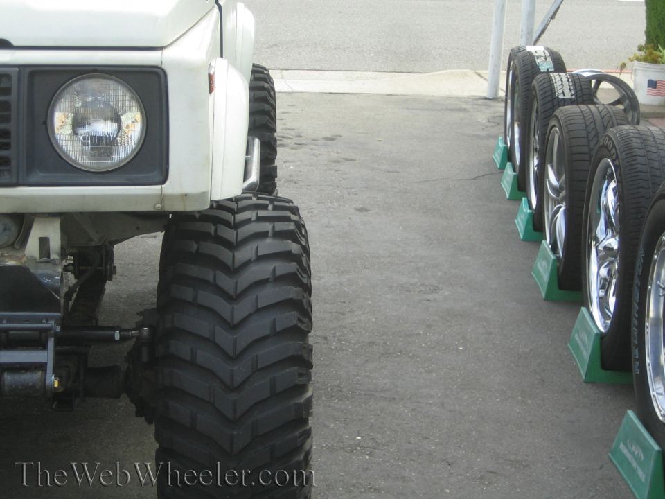 Low view of white 4x4 front corner with large lug mud tire beside tire shop display