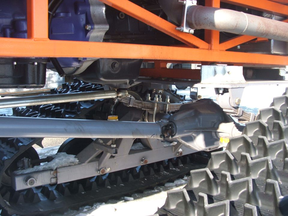 Undercarriage of tracked vehicle with orange frame, blue engine, and leaf springs