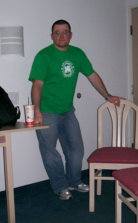 1990 Ford Bronco - A man stands in a room, wearing a green t-shirt and jeans, with a drink on a nearby table.